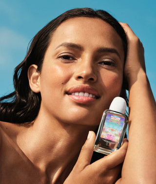 Perfume bottle labeled "Solar Canopy" held by female model with blue sky background