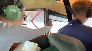 October 2021. Two people in a plane, our pilot Kenn and my colleague Jaide, who is sticking her hand out the window with a petri dish. 