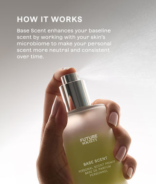 A hand with manicured nails holds a frosted glass bottle of Future Scent Base Scent personal scent primer, spraying a fine mist. The background is a soft light gray with white text explaining how the product works. Base Scent enhances your baseline scent by working with skin's microbiome to make your personal scent ore neutral and consistent over time.