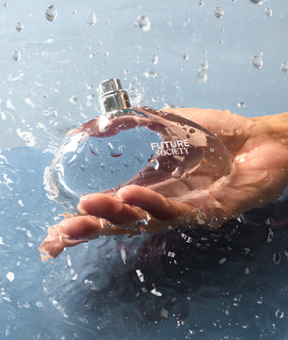 Hand holding a clear perfume bottle labeled 'Future Society' with rain droplets around it.