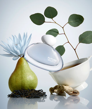 Perfume bottle labeled 'Future Society' with a pear, plant, and bowl on a reflective surface.